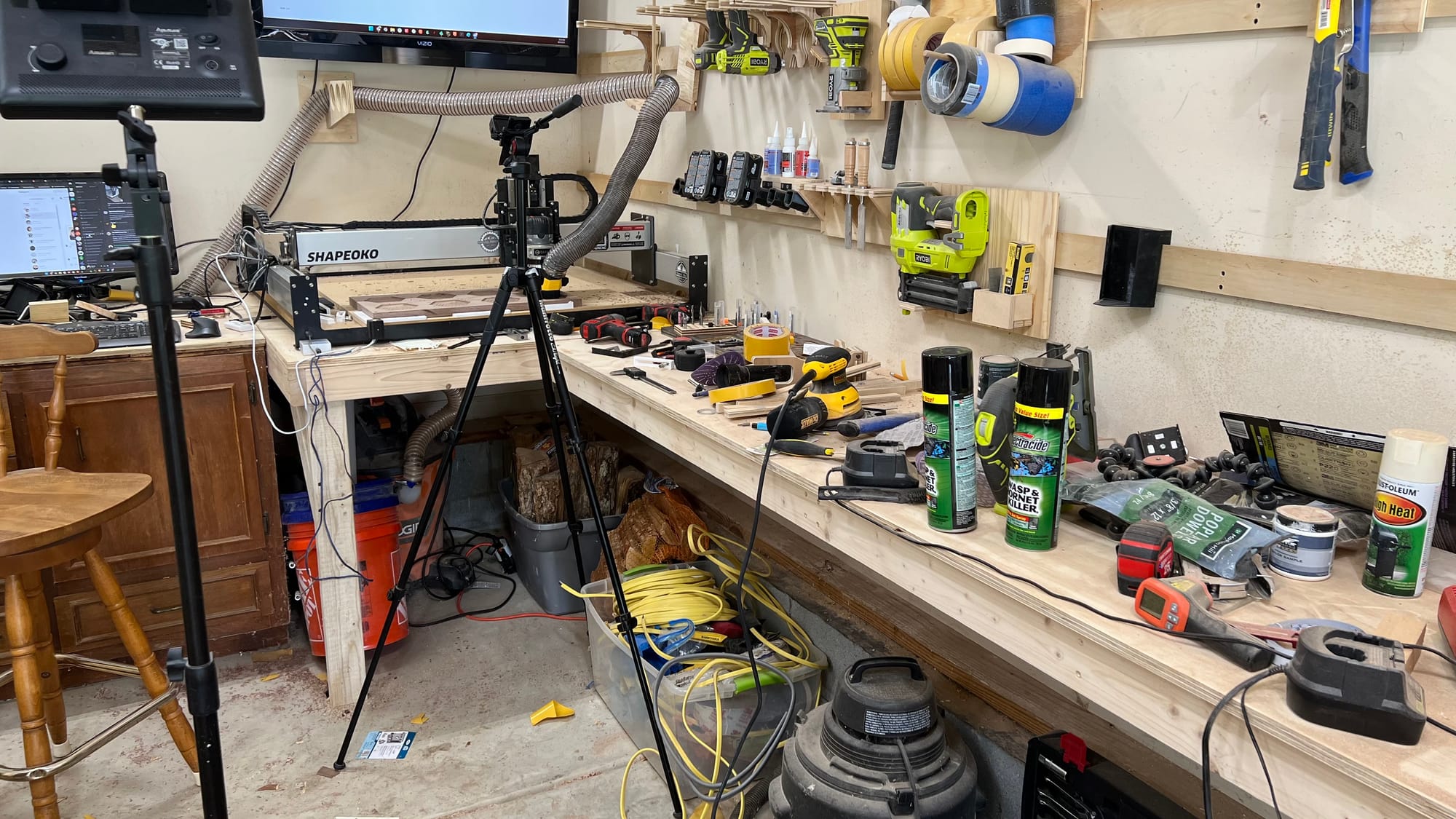 A messy workshop with tools everywhere, lighting and camera equipment set up.