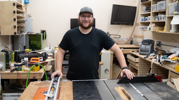 Patrick Campanale of Created Workshop standing in his workshop in front of a table saw with lasers behind him.